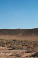 Barren desert landscape is pictured, showcasing a rocky terrain with a few goats in the distance