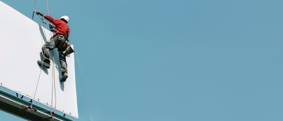 A technician man is suspended on the edge of an advertising billboard still working with safety equipment and a helmet, The sky behind him is blue, Generative AI