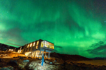 Aurora borealis, Northern lights glowing over luxury hotel and male tourist enjoying on mount Hengill in winter at Iceland