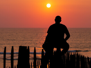surfer assis sur une barrière à contre-jour en attendant une vague devant la mer au coucher du...
