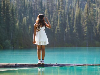 Young female in a white summer dress standing on the lake surface with vegetation in the background