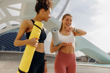 Smiling woman with female friend looking on smartwatch before exercising standing outdoors