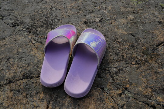 Pink or purple slippers outside during the summer. Rocky background.