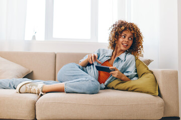 Cozy Home Comfort: Woman Holding Mobile Phone, Relaxing on Sofa, Smiling Happily while Reading and Chatting Online in a Living Room.
