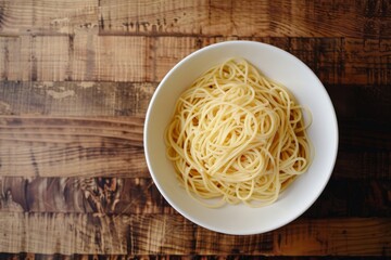 Top-down view of a white bowl filled with pasta on a wooden table
