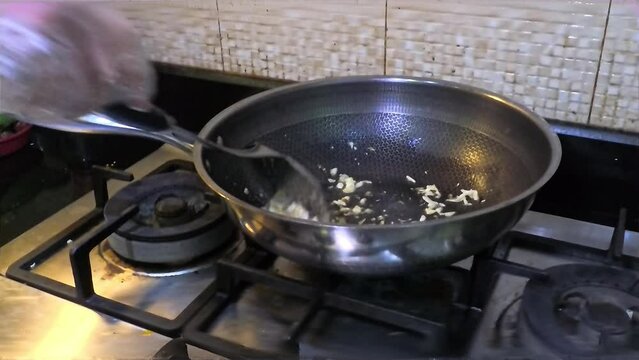A cook is frying fried garlic with vegetable oil in a pan, in his kitchen.