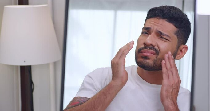 A handsome young man is worried about the wrinkles on his face while looking in the mirror.