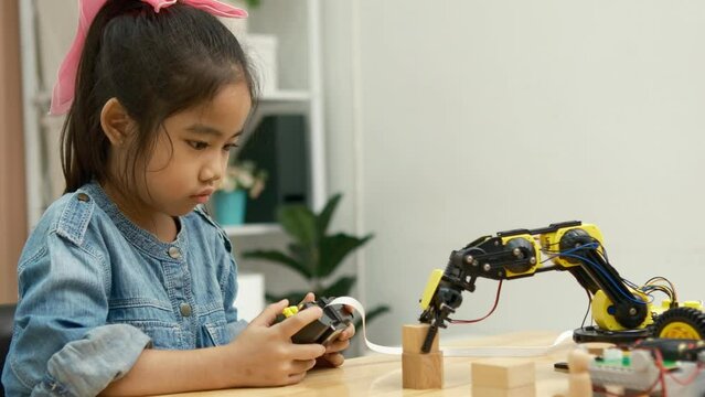 A primary school girl focuses on operating a robotic arm with a remote control, demonstrating STEM education in action.