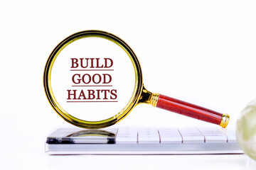 BUILD GOOD HABITS motivational concept text through a magnifying glass on a calculator on a light background