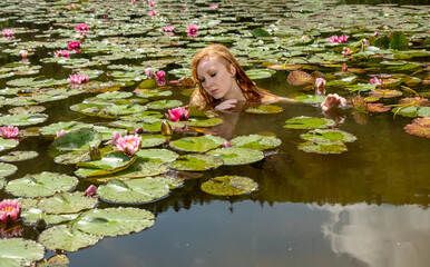 young sexy naked redhead mermaid woman swims sensual seductive in the water, lake, pond, with pink water lilies