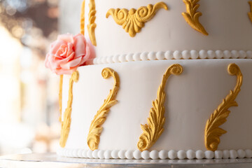 ornate wedding cake with gold scrollwork and a pink rose