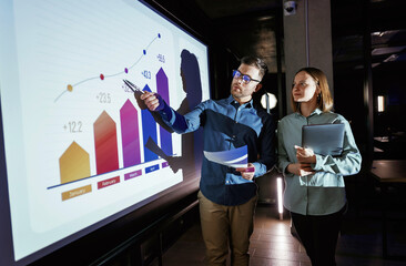 Conception of profit. Man and woman are standing near projector with business data, cooperation