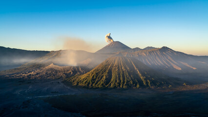 Volcano spewing smoke into sky among natural mountain landscape - obrazy, fototapety, plakaty