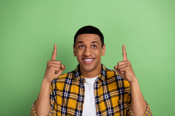 Photo of young hipster smiling guy in yellow shirt directing fingers up empty space his favorite...