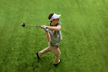 Skilled, focused on game golfer from above at end of swing posing on lush green golf court. Male model looking at distance. Concept of professional sport, luxury games, active lifestyle, action. Ad