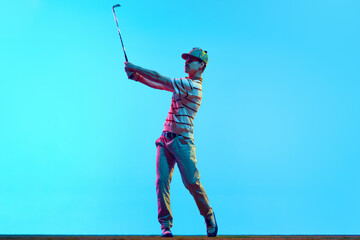 Full length portrait of golfer hitting golf shot with club on course in neon light against gradient...