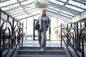 Attractive and stylish mature woman in grey pant suit with jacket and turtleneck, accessorized with...