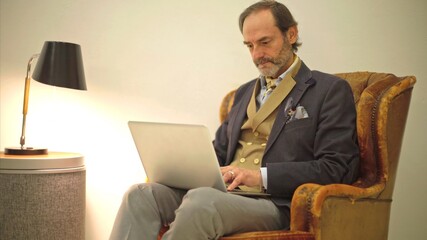 Mature man working on laptop in vintage armchair.