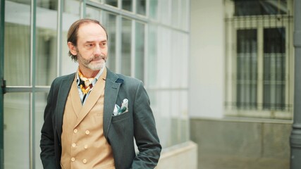 Elegant senior man in a waistcoat standing by glass building
