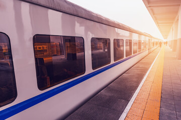 Passenger train stands by the platform at sunset.