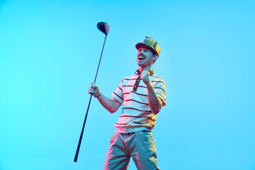 Joyful golfer in retro outfit and cap celebrating perfect goal with raised fist and golf club in...