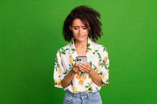 Photo of unsure unhappy lady wear print shirt biting lip getting message modern device isolated green color background