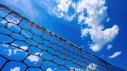 A close-up of a tennis net against a backdrop of vibrant blue sky and fluffy white clouds. 