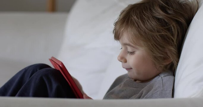 Happy kid boy using tablet on sofa.