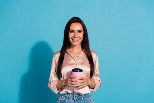 Photo of positive lovely girl with straight hairdo wear silk blouse holding cup of latte in hands isolated on blue color background