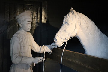 A man takes care of a horse in a stall, marble figures.
