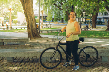 happy middle-aged latin woman standing next to her bike in a park smiling with vitality. copy space