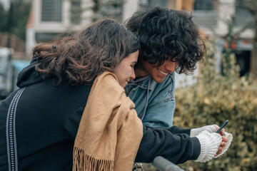 Beautiful young couple in love walking outdoors at the city street, using mobile phones