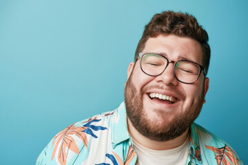 A delighted man with fashionable eyewear is grinning broadly in front of a uniform blue background, radiating warmth - obrazy, fototapety, plakaty