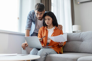Household papers problem. Indian couple looking at laptop and holding documents, reading bills and...