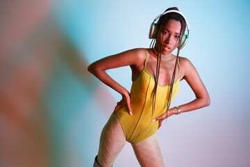 young african american woman in headphones posing in yellow bodysuit with hands on hips in studio