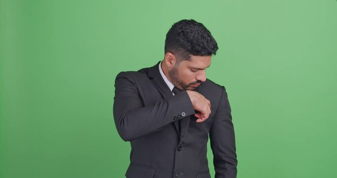 Asian businessman in a black suit takes something out of his suit pocket. Isolated on green background in studio.