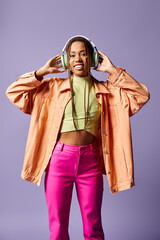 happy african american girl in wireless headphones and vibrant casual attire on purple background