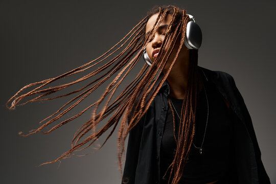 ecstatic dance of carefree african american girl with dreadlocks and wireless headphones on grey
