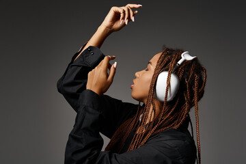 artistic african american girl in 20s with dreadlocks listening music in headphones on grey backdrop