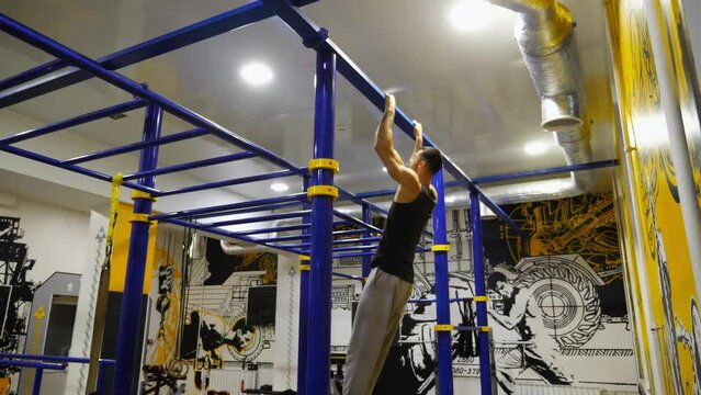 Young muscular athlete showing performance on horizontal bar at modern gym. Strong sporty man doing some gymnastics stunts on sports equipment at fitness centre. Concept of sportive lifestyle. Slow mo