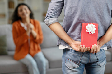 Husband congratulating hindu wife, holding wrapped present box behind back celebrating romantic...