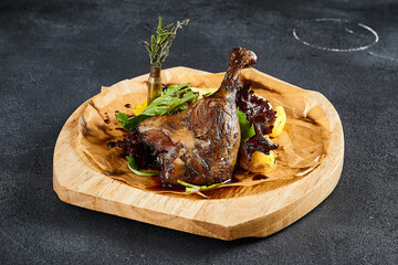 Duck leg confit with baked apples, presented on a wooden cutting board, top view. A delicious...