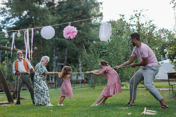 Grandparents have a tug of war with their grandkids. Fun games at family garden party.