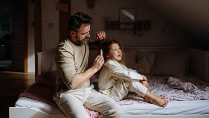 Father combing and braiding daughter's hair as part of bedtime routine. Single dad taking care of his daughter's hairstyle.