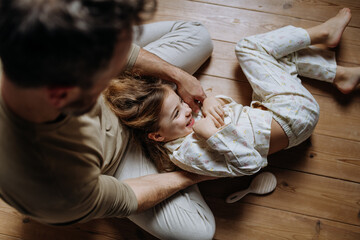 Top view of father with daughter on floor laughing together, having fun, tickling each other. Girls...