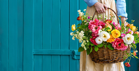 A woman is holding a wicker basket full of garden flowers. Floral gardening concept