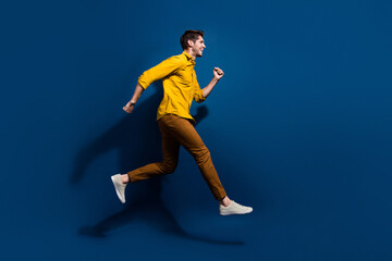 Fototapeta na wymiar Full body photo of handsome young guy jump running hurry shopping dressed stylish yellow outfit isolated on dark blue color background