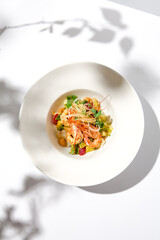 Elegant food - salad with shrimp and avocado on white table with harsh shadow. Flashy food concept. Seafood salad with shrimp, tomatoes and avocado on white plate with sunlight.