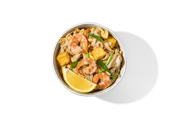 Traditional asian street food - pad thai noodles with shrimp, vegetables and tofu isolated on white background. Pad thai udon with prawns and lemon in ceramic bowl. Fried udon noodles with seafood.