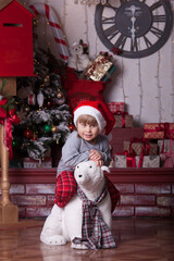 A portrait of a little girl in a red Santa hat is sitting on an artificial white bear (red, white and gray Christmas interior)
